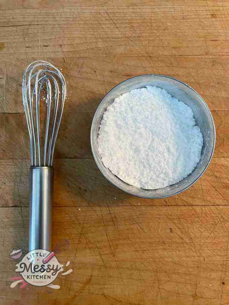 Powdered sugar and cornstarch mixture in a bowl with a mini whisk beside it.