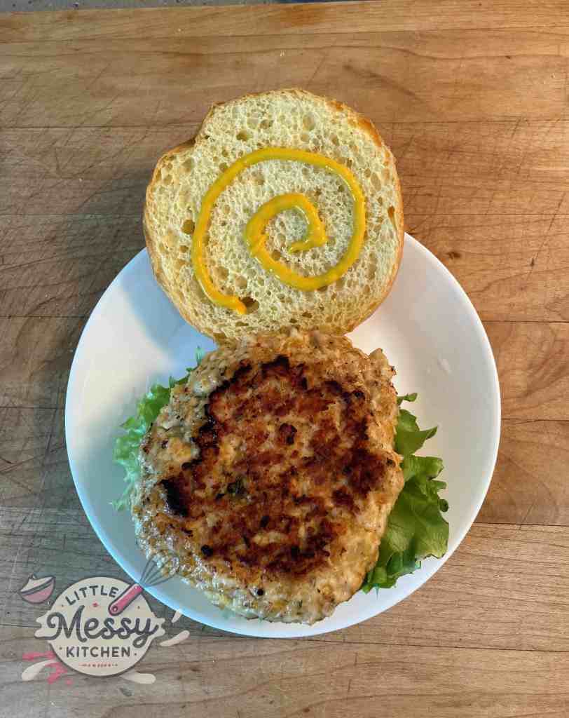 Chicken patty on opened burger bun, with mustard on top bun.