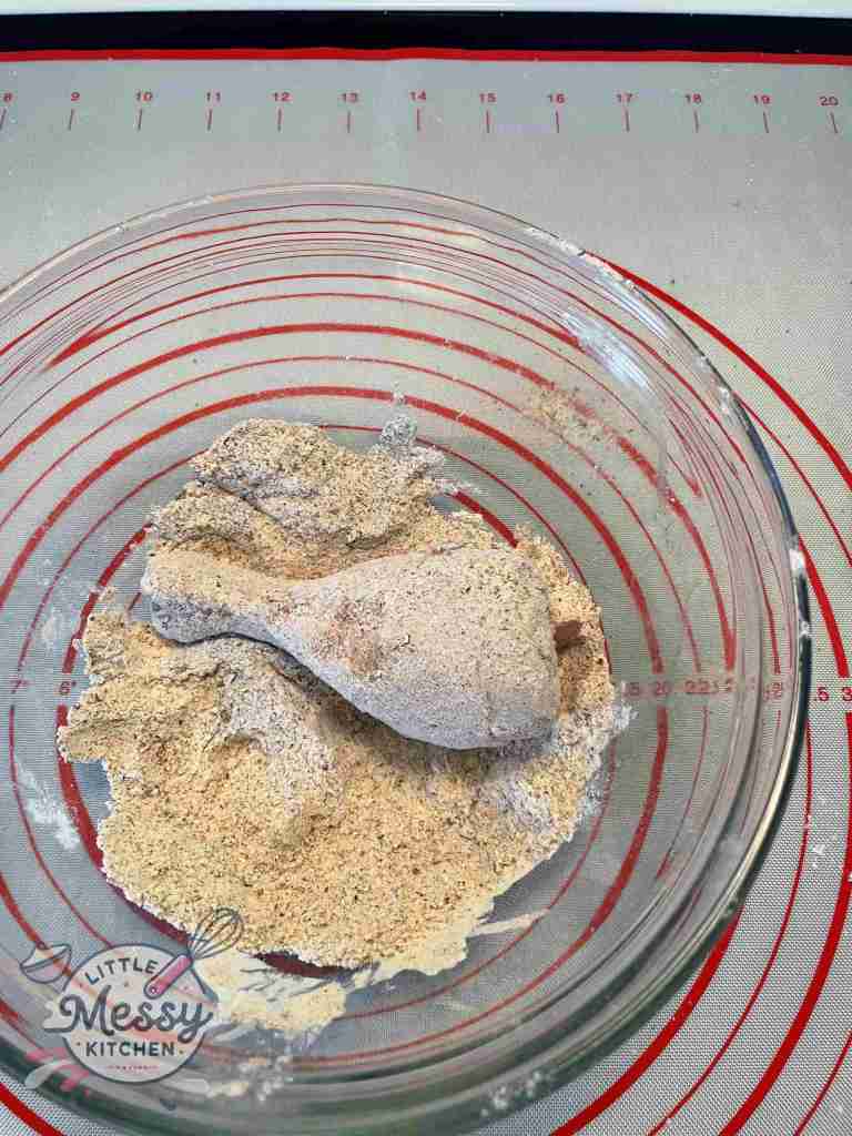 Chicken drumstick coated with flour and spice mixture in a bowl.