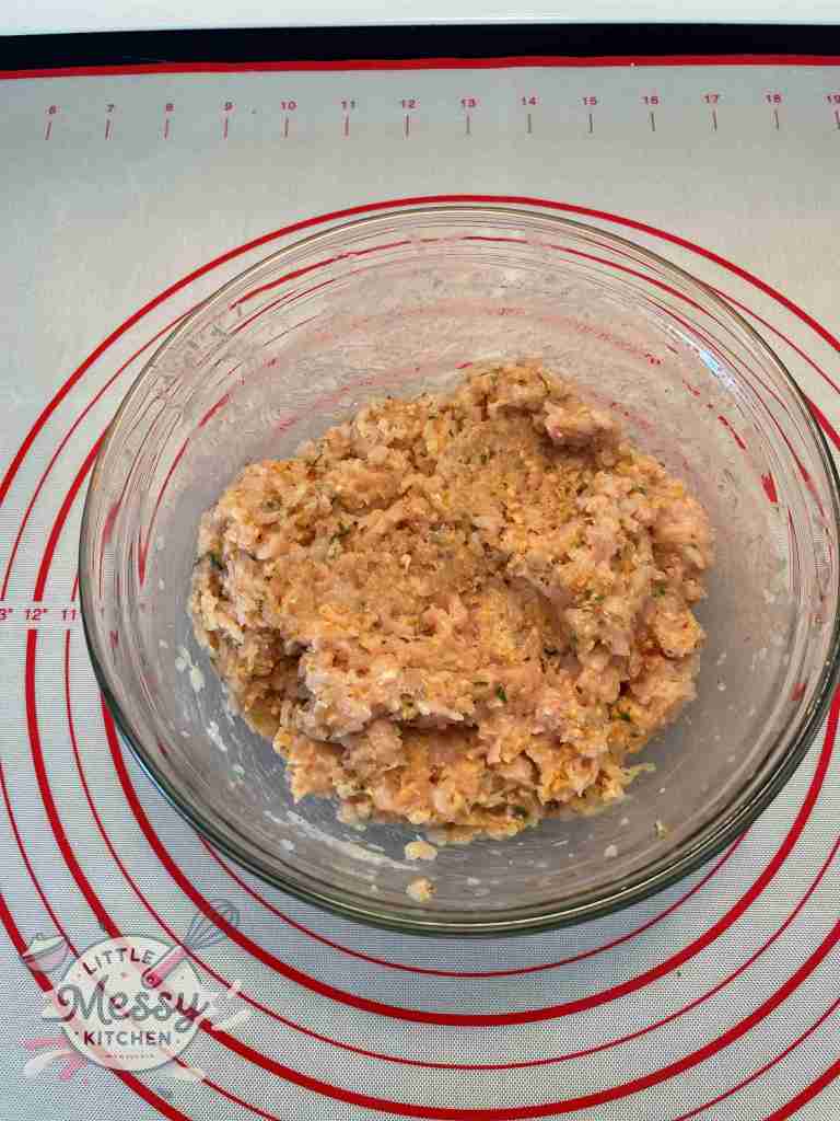 Ground chicken breast, Italian breadcrumbs, mayonnaise, minced onions, chopped parsley, minced garlic, paprika, salt, and black pepper, well mixed in a bowl.