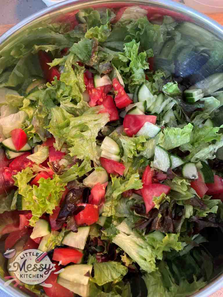 Red and green lettuce, with tomato and cucumber slices in a bowl.