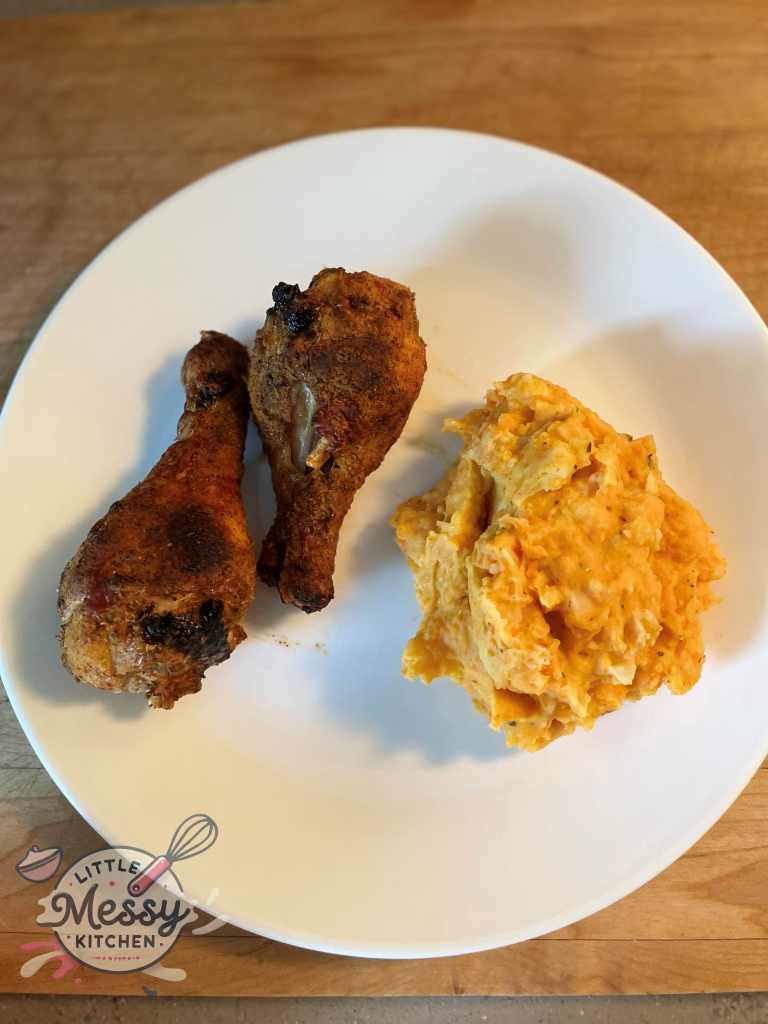 Portion of mashed potatoes and carrots on a plate with two crispy chicken drumsticks.