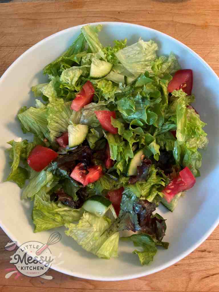 Red and green lettuce, with tomato and cucumber slices in a serving bowl.