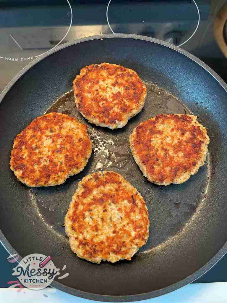 4 chicken patties cooking in a frying pan.