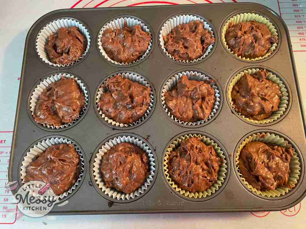 Muffin pan lined with muffin cups filled with batter.