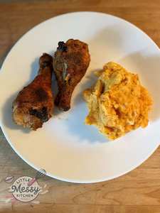 Portion of mashed potatoes and carrots on a plate with two crispy chicken drumsticks.