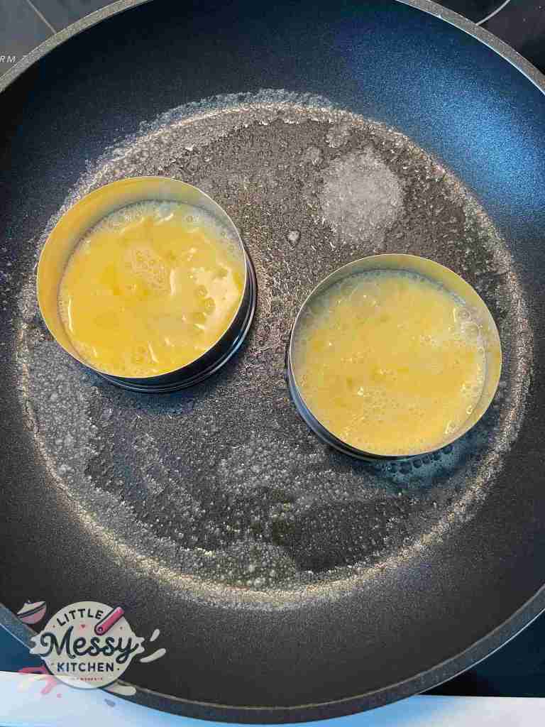Two eggs cooking in a skillet with round cookie cutters to keep them perfectly shaped.