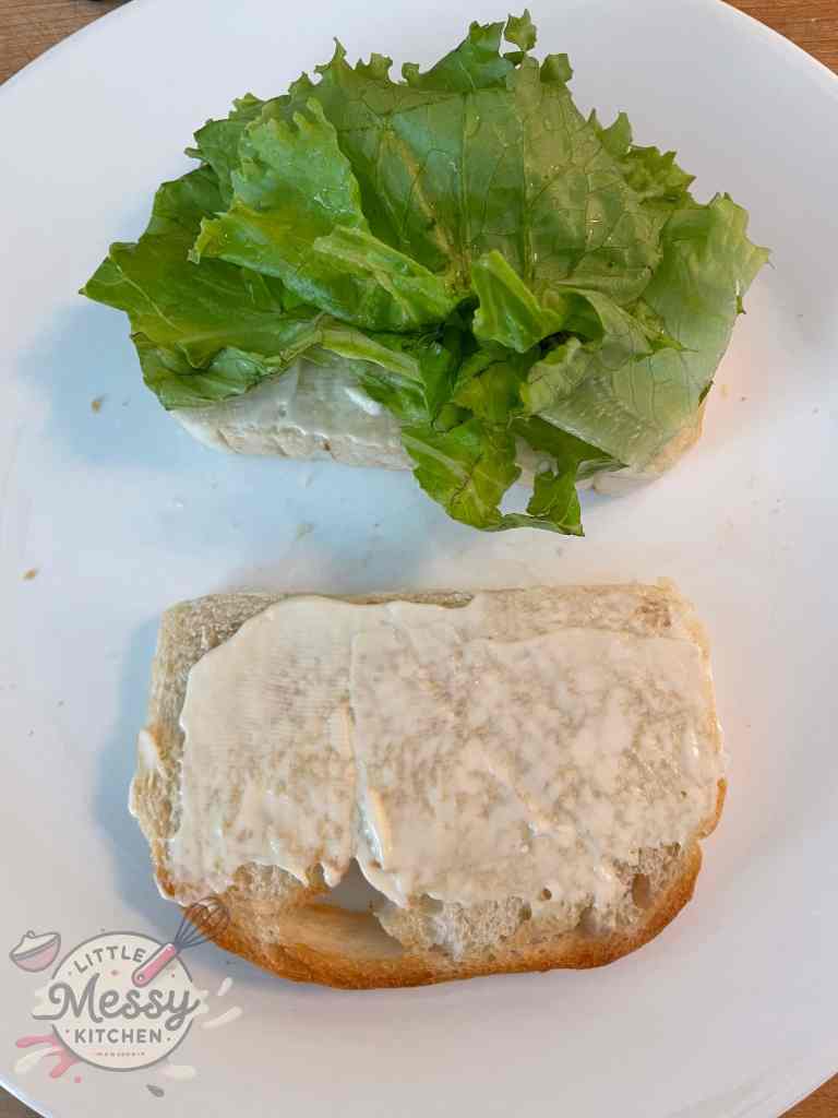 Open-faced sandwich with one slice of bread topped with fresh lettuce and the other slice spread with mayonnaise, ready for assembly.