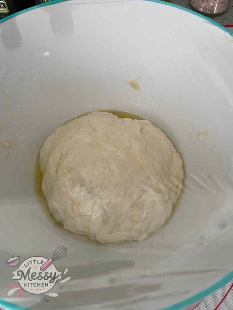 Homemade pita bread dough resting in a white bowl, coated with olive oil, and ready to rise for fresh, fluffy pita bread.