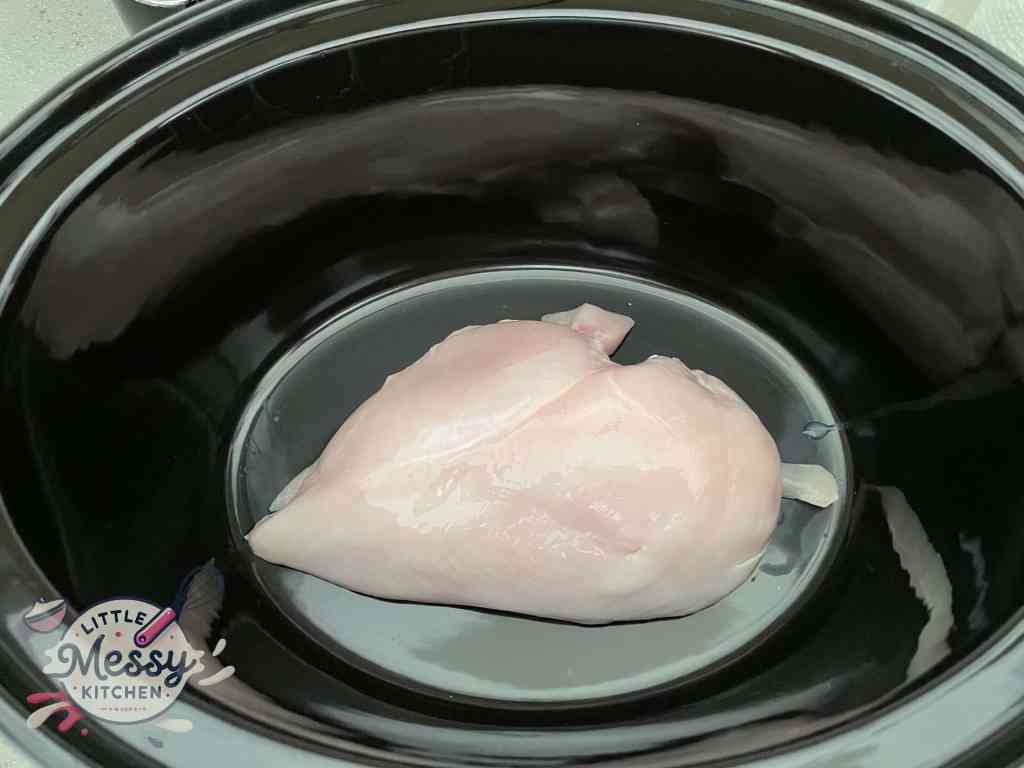 Uncooked chicken breast placed in a slow cooker.