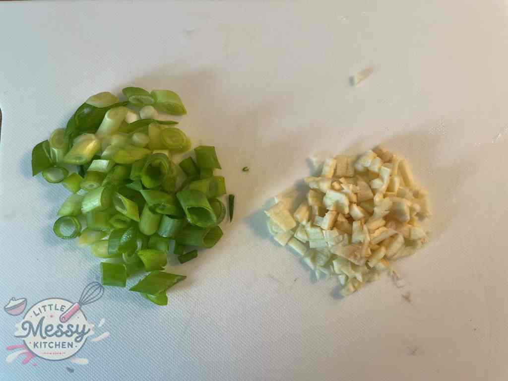 Sliced green onions and garlic on a cutting board, ready for cooking.