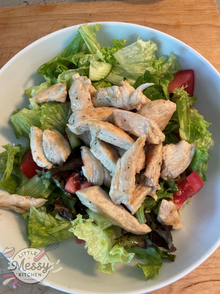 Serving of green salad base topped with cooked chicken.