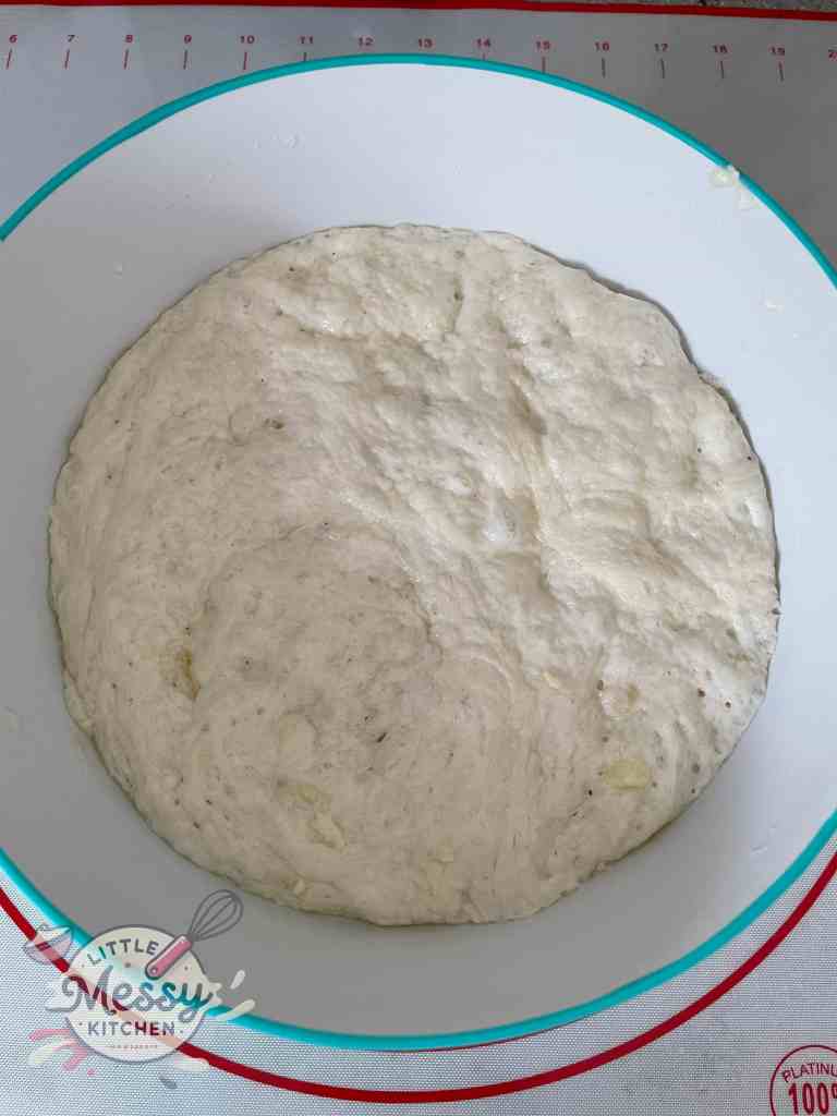 Risen homemade pita bread dough in a white bowl, ready to be portioned and baked into fluffy pita bread.