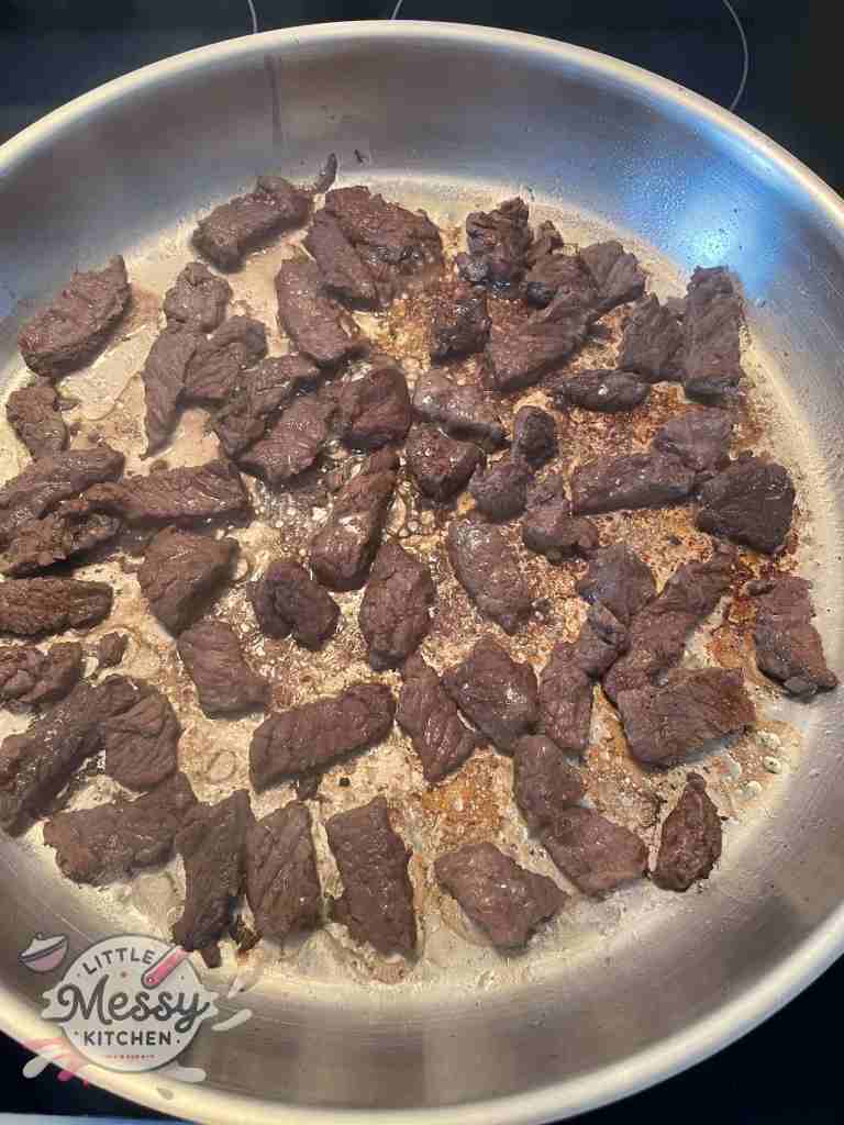 Bite size steak pieces searing in frying pan.