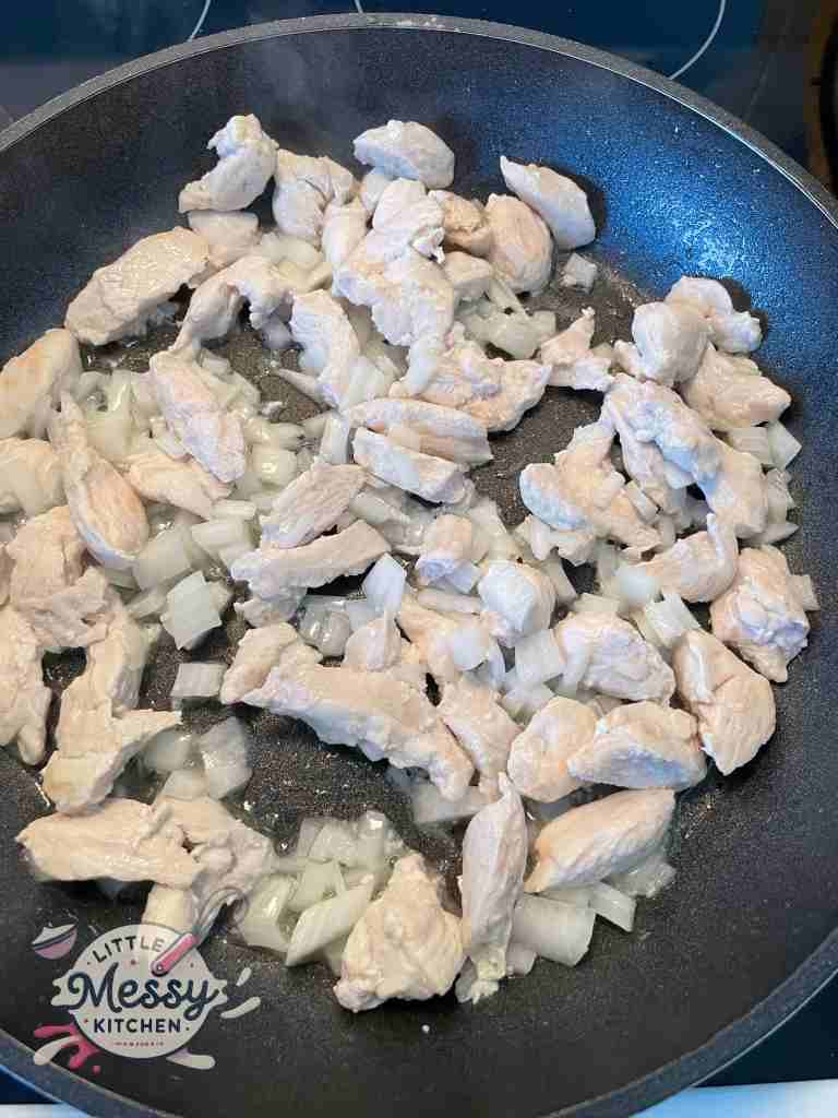 Sliced chicken and diced onions cooking in frying pan.