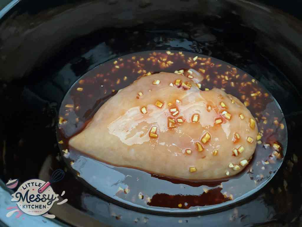 Sauce poured over chicken breast in a slow cooker, ready for cooking.
