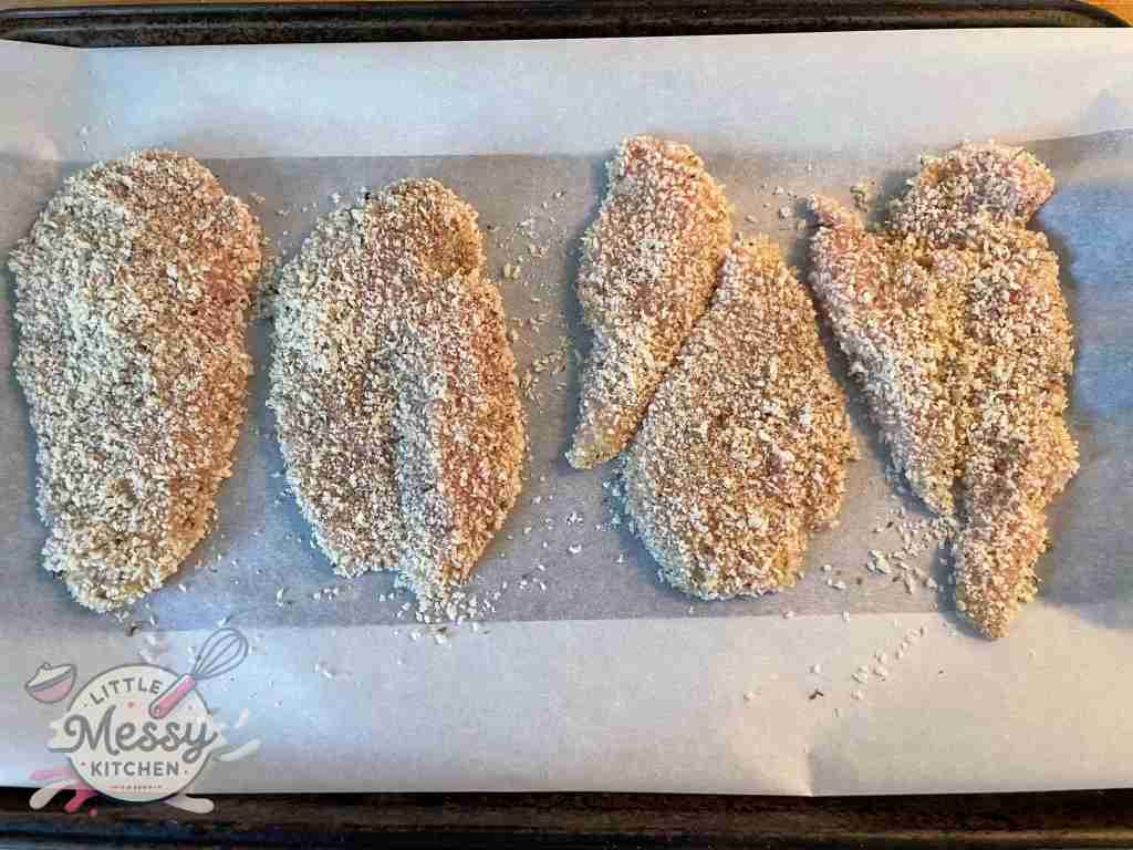 Breaded chicken breast on a baking sheet ready to be cooked.