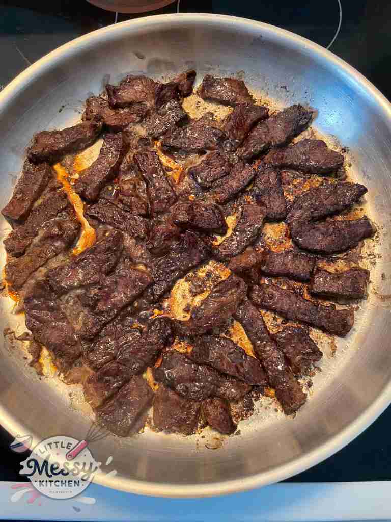 Marinated steak cooking in frying pan.