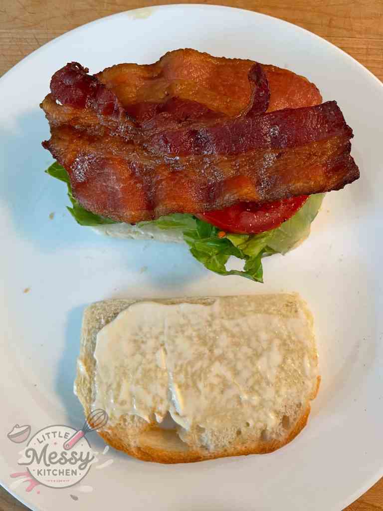 Open-faced sandwich with one slice of bread topped with lettuce, tomato slices, and crispy bacon, and the other slice spread with mayonnaise, ready for assembly.
