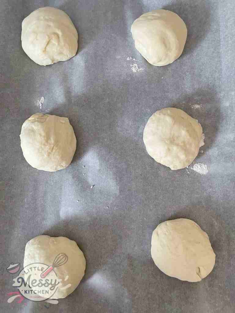 Six portioned balls of homemade pita bread dough resting on parchment paper, ready to be rolled out and baked.