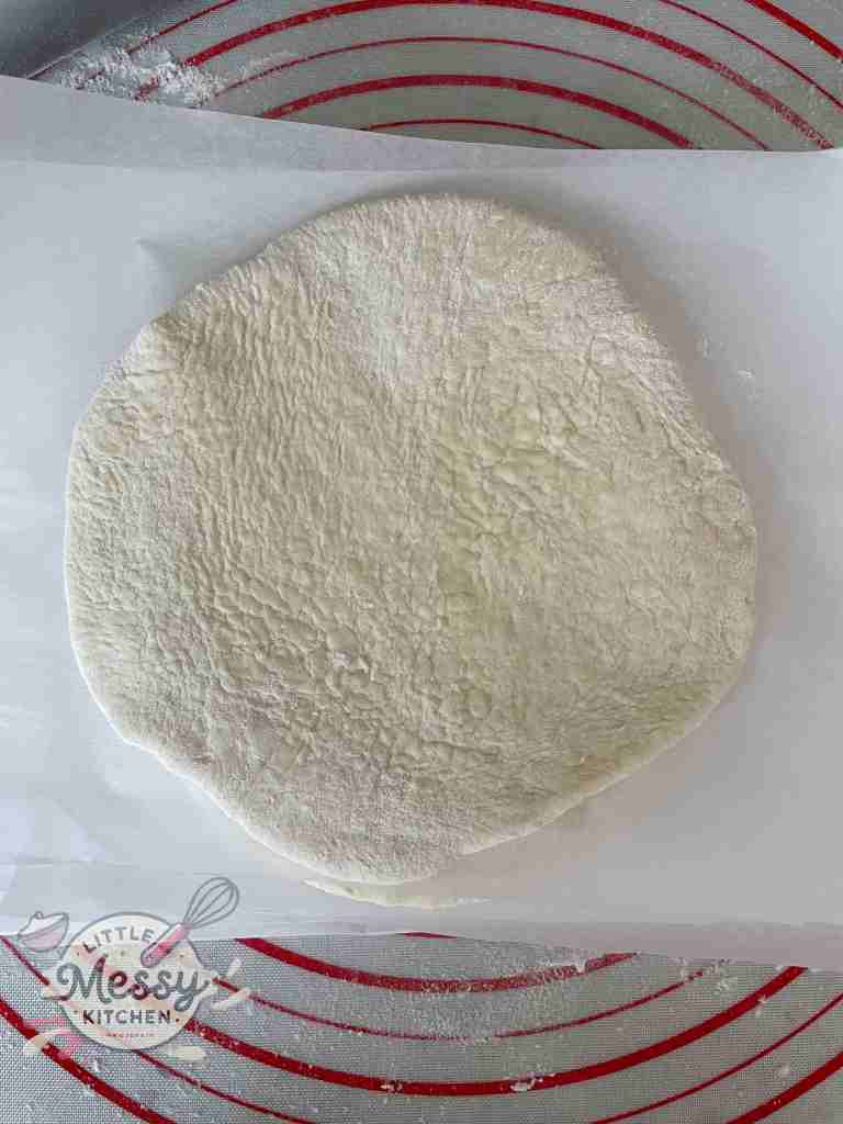 Rolled out homemade pita bread dough resting on parchment paper, ready to be baked into soft, fluffy pita bread.