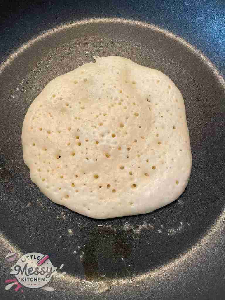 Pancake in a skillet with bubbles forming on the uncooked side.