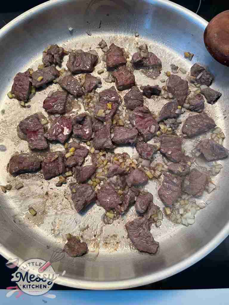 Sirloin steak bite sized cooking in frying pan with garlic and ginger.
