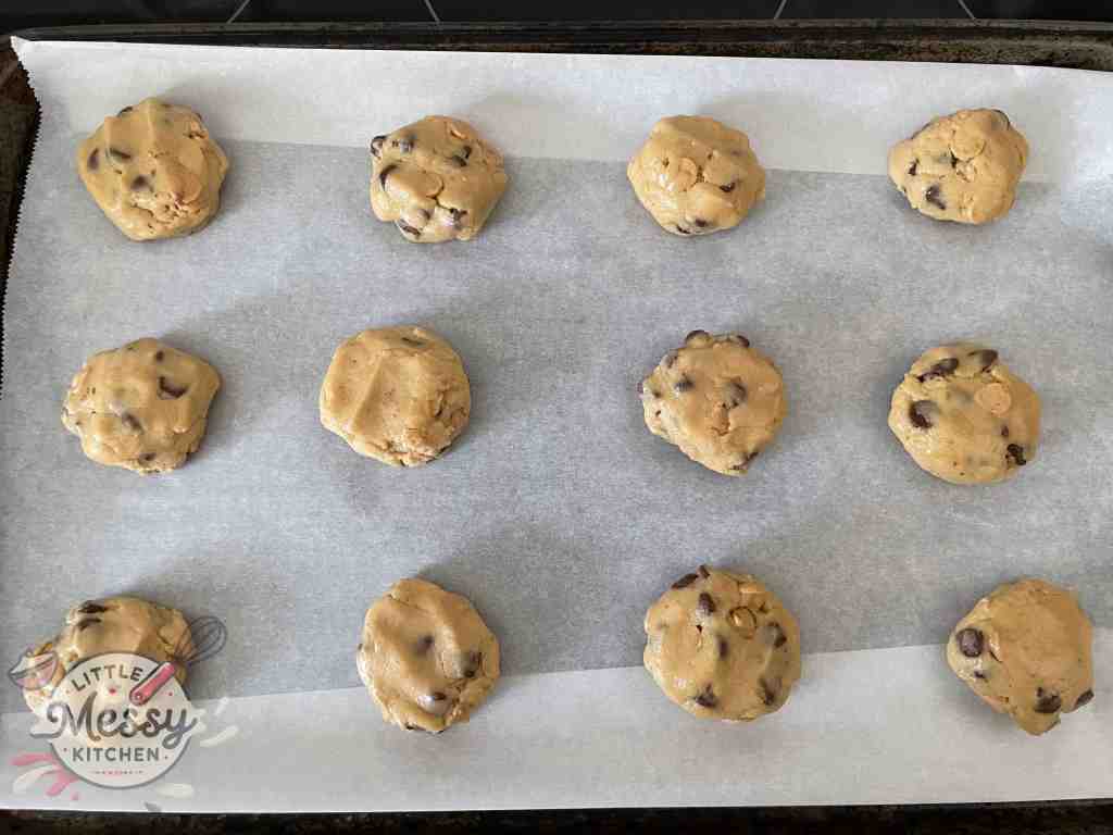 Unbaked chocolate chip cookie dough balls placed on a parchment-lined baking sheet, ready to be baked in the oven.