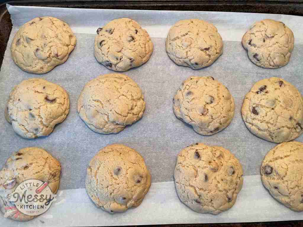 Freshly baked chocolate chip cookies cooling on a parchment-lined baking sheet, with a golden-brown surface and a soft, chewy texture.
