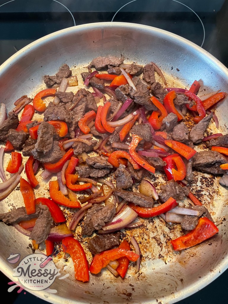 Steak, Red bell pepper and onion slices sauté in frying pan.