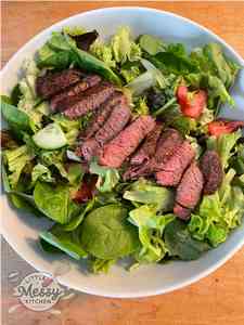 Serving of green salad base topped with sliced steak.