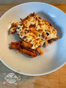 A serving of baked pasta with melted cheese on top, placed in a white bowl.