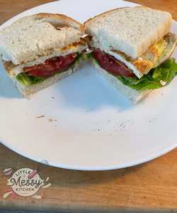Completed BELT sandwich cut in half, showing layers of lettuce, tomato, bacon, and egg between slices of bread, served on a white plate.