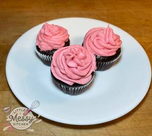 Chocolate cupcakes with pink raspberry buttercream frosting on a white plate.
