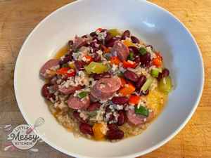 A bowl of Sausage, Red Beans, and Rice Casserole served hot, featuring slices of andouille sausage, red kidney beans, diced bell peppers, celery, and onions mixed with rice, garnished with a light broth.