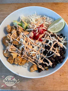 Marinated chicken, black beans, avocado, tomato and slice of lime on a bed of rice with taco sauce drizzled on top.