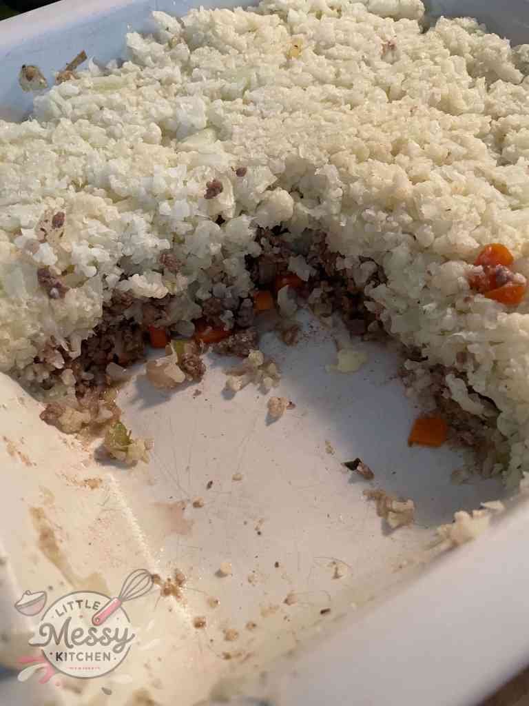 Partially served Low-Carb Beef & Cauliflower Bake in a white baking dish, showing the layers of ground beef, vegetables, and mashed cauliflower topping.