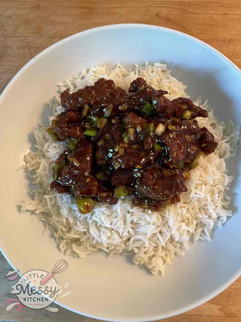 Serving of Mongolian beef on a bed of rice in a white bowl.