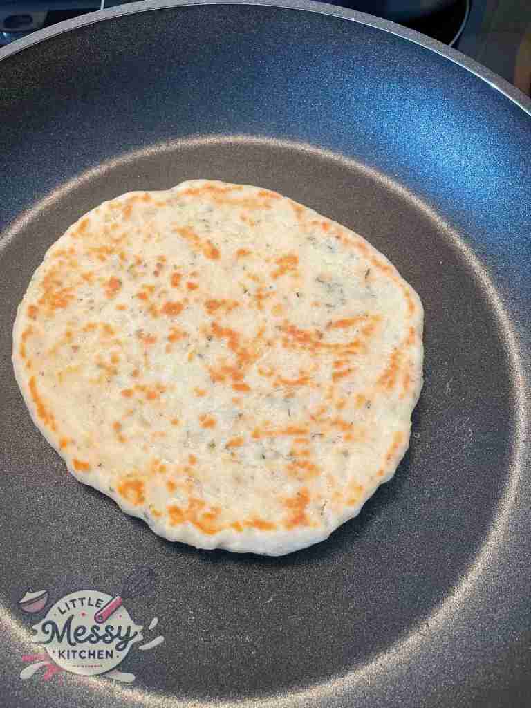 Flatbread cooking in frying pan on second side.