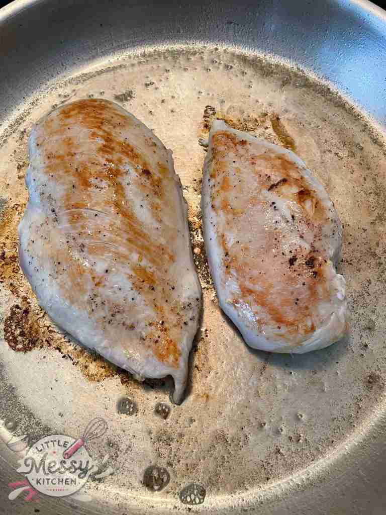 Chicken breast cooking in frying pan.
