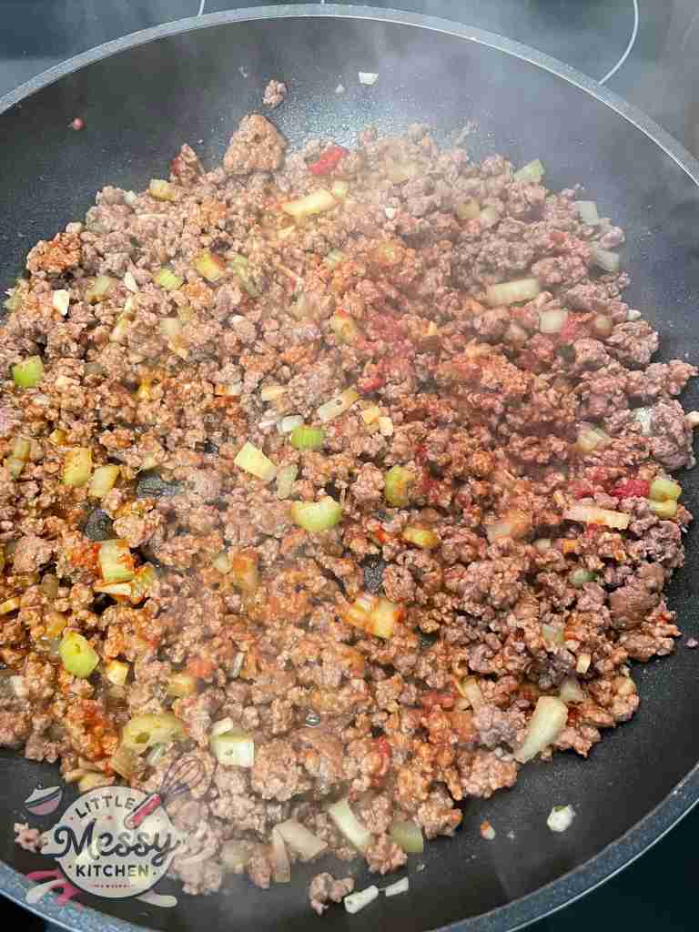 Ground beef, diced celery, minced garlic and tomato paste cooking in skillet.