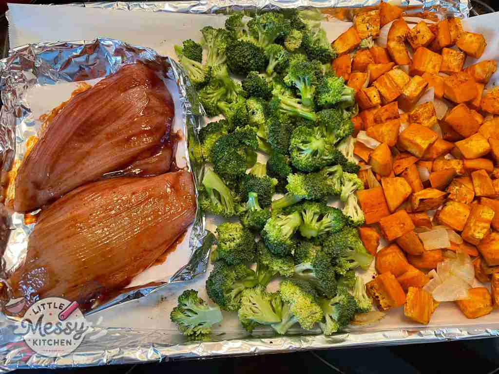 Sweet Potato and onions, broccoli floret and chicken breast on a baking sheet.