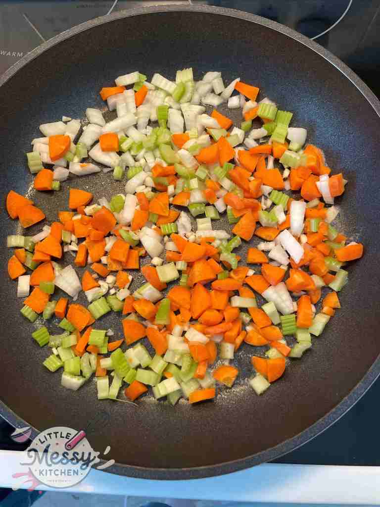 Diced Onion, carrots, celery, and garlic sauteing in a skillet.