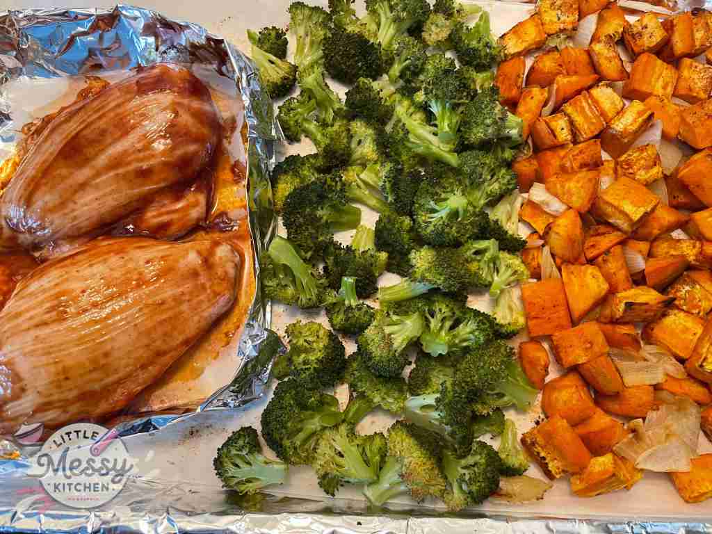Sweet Potato and onions, broccoli floret and chicken breast on a baking sheet.