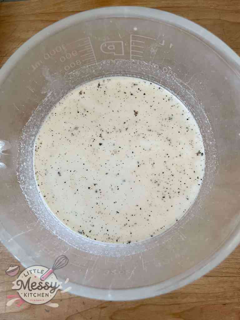 Chicken stock, milk, dijon, and pepper, mixed in a glass measuring cup.