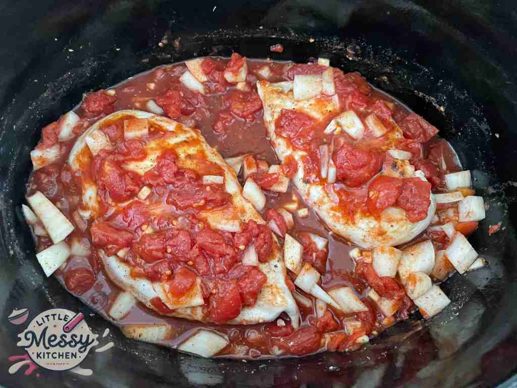 Chicken breast resting on tomato mixture in slow cooker.