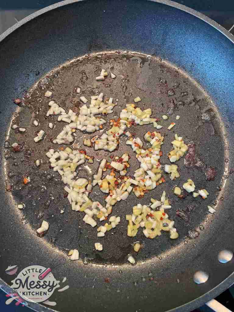 Garlic, ginger and red pepper flakes saute in a frying pan.