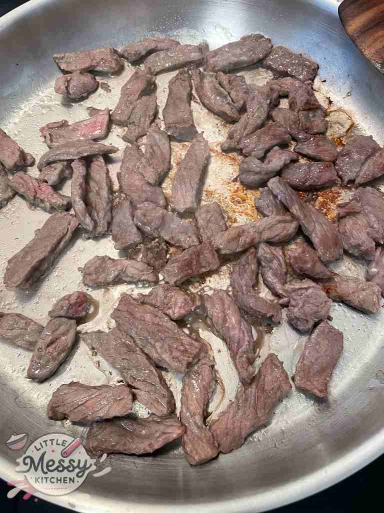 Steak slices cooking in frying pan.