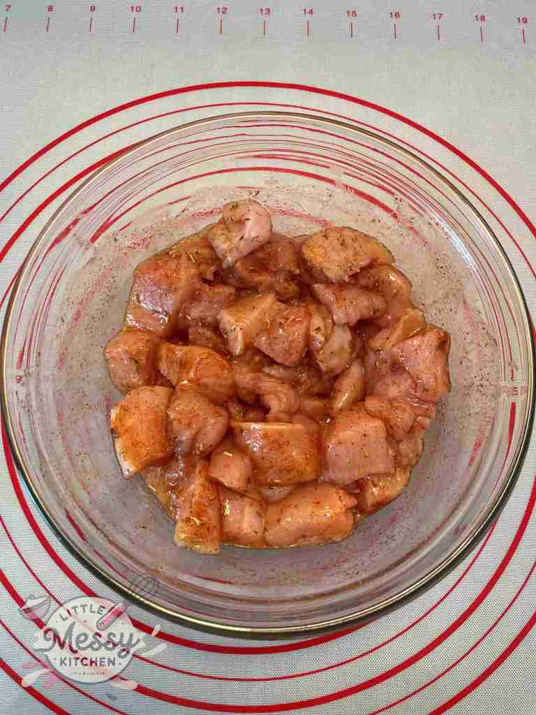 Chicken pieces seasoned with Spices and Olive Oil in a mixing bowl.