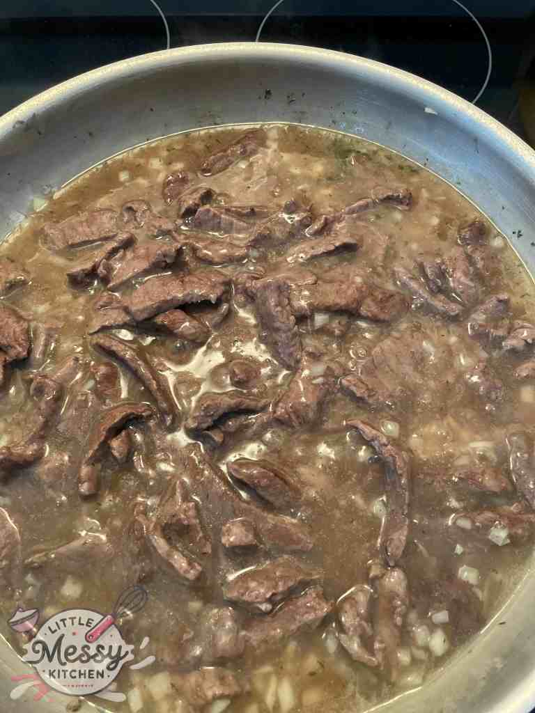 Steak strips added to the sauce in skillet.